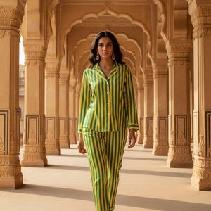 Peut inclure: Une personne porte un ensemble de pyjama &agrave; rayures vertes et jaunes. La chemise boutonn&eacute;e &agrave; manches longues et le pantalon assorti pr&eacute;sentent des rayures verticales. Le pyjama est bord&eacute; d'une couleur contrastante. L'arri&egrave;re-plan pr&eacute;sente une colonnade avec des plafonds vo&ucirc;t&eacute;s.