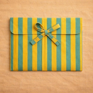 Peut inclure: Pochette rectangulaire en tissu &agrave; rayures verticales turquoise et jaune, ferm&eacute;e par un n&oelig;ud assorti. Le fond est une surface textur&eacute;e brun clair.