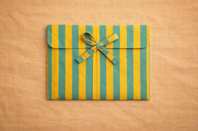 Peut inclure: Pochette rectangulaire en tissu &agrave; rayures verticales turquoise et jaune, ferm&eacute;e par un n&oelig;ud assorti. Le fond est une surface textur&eacute;e brun clair.