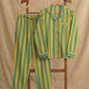 Peut inclure: Ensemble de pyjama &agrave; rayures jaunes et turquoise. La chemise boutonn&eacute;e &agrave; manches longues et le pantalon assorti sont pr&eacute;sent&eacute;s sur un cintre en bois. Le pyjama a des bordures blanches et une taille &agrave; cordon. L'ensemble est en tissu doux et l&eacute;ger.