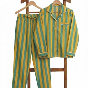 Peut inclure: Un ensemble de pyjama &agrave; rayures verticales jaunes et vertes. L'ensemble comprend une chemise &agrave; manches longues et un pantalon, avec des bordures blanches. Le pyjama est pr&eacute;sent&eacute; sur un cintre en bois.