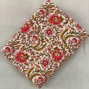 Op de afbeelding: Gevouwen stof met een bloemenpatroon. De stof heeft grote, roze en rode bloemen met groene bladeren en stelen op een witte achtergrond. Het bloemmotief wordt herhaald over de stof.