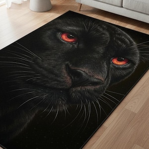 May include: Black panther rug featuring a close-up of the animal's face. The panther's fur is black, with long white whiskers and intense red eyes. The rug is rectangular and placed on a wooden floor.