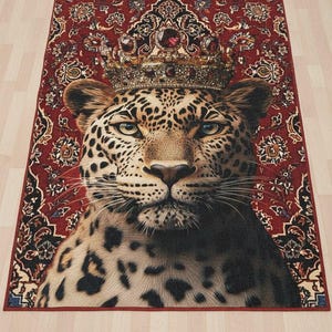 May include: A rectangular rug featuring a regal leopard wearing a jeweled crown. The leopard has a spotted coat and is set against a red patterned background. The rug's border is a darker shade of red.