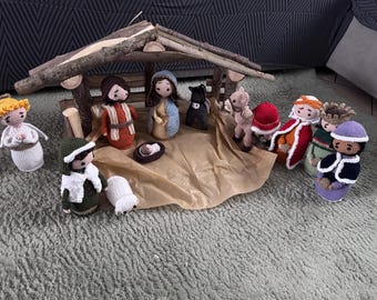 May include: A handmade crochet nativity scene featuring figures like Mary, Joseph, baby Jesus, angels, and the Three Wise Men. The scene includes a wooden stable and is set on a brown paper base. The figures are in various colors.