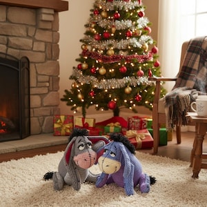 May include: Two crocheted donkey plush toys, one gray and one blue, sit on a cream-colored rug in front of a decorated Christmas tree. The tree is adorned with ornaments, lights, and garland. Wrapped gifts are placed beneath the tree.