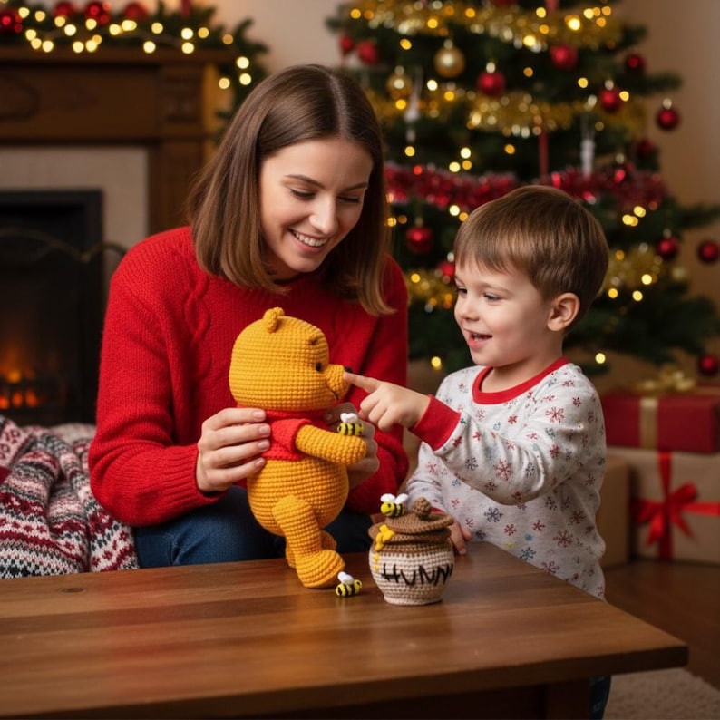 May include: A crocheted Winnie the Pooh doll in yellow with a red shirt, held by a person. A child points at the doll's nose. A crocheted honey pot with bees and the word "HUNNY" is on the table. Christmas tree in the background.