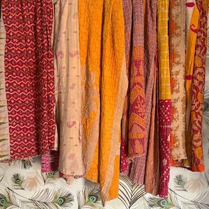 May include: A display of vibrant, patterned textiles, possibly blankets or throws, suspended against a patterned wallpaper. The fabrics showcase a range of warm hues, such as red, orange, and yellow, with detailed designs and textures.