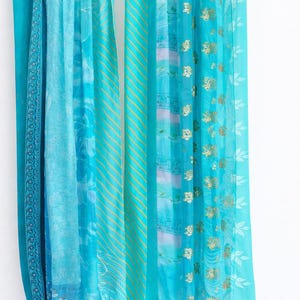 May include: A set of turquoise curtains with varying patterns and textures. The curtains are hung on a silver rod with green clips. The fabrics include stripes, floral designs, and gold accents, creating a layered and decorative effect.