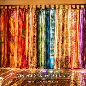 May include: A series of hanging curtains made from vintage silk saris in a vibrant spectrum of colors including orange, red, green, blue, and purple. The panels feature diverse floral and geometric patterns, suspended from a dark rod with tabs.