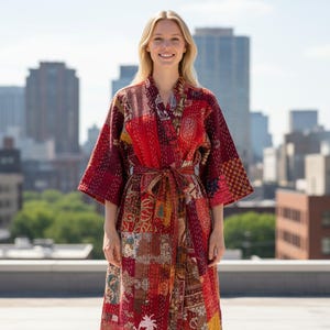 May include: A patchwork robe in shades of red, burgundy, and gold. The robe features a wrap-around design with a tie closure at the waist. The fabric is a mix of patterned and solid pieces, creating a unique, bohemian style. The robe is worn by a person.