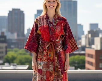 May include: A patchwork robe in shades of red, burgundy, and gold. The robe features a wrap-around design with a tie closure at the waist. The fabric is a mix of patterned and solid pieces, creating a unique, bohemian style. The robe is worn by a person.