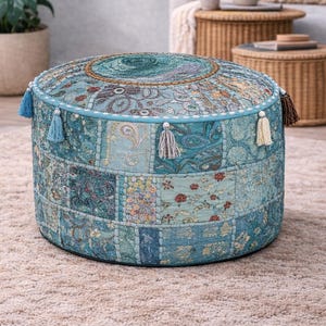 Könnte beinhalten: Ein runder Patchwork-Pouf in Türkis-, Blau- und Beigetönen. Der Stoff ist mit Paisley- und Blumenmustern versehen. Der Pouf hat eine dekorative Bordüre und Quasten in verschiedenen Farben.