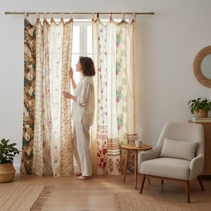 Puede incluir: Cortinas estampadas en tonos beige, marrón y rojo cuelgan frente a una ventana. Las cortinas presentan diseños florales y geométricos. Una mujer está de pie cerca de la ventana. Un sillón beige y una pequeña mesa de madera están en la habitación.