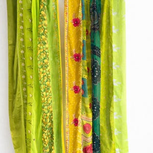 Peut inclure: Rideaux en tissu colorés suspendus à une tringle métallique. Les rideaux présentent divers motifs, notamment des motifs floraux et des couleurs unies dans des tons de vert et de jaune. Les rideaux sont faits d'un matériau léger.