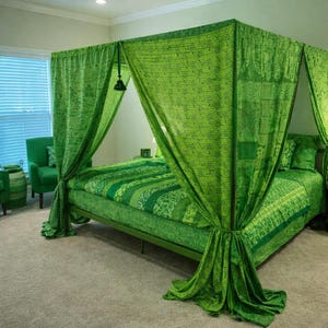 Puede incluir: Una cama con dosel verde con ropa de cama y cortinas a juego. El marco de la cama y los muebles circundantes también son verdes, creando un conjunto de dormitorio cohesivo y vibrante. Las cortinas están drapeadas alrededor de los postes de la cama.