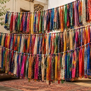 May include: A large collection of colorful silk scarves hanging in multiple rows on horizontal lines. The scarves feature a wide variety of vibrant patterns, floral prints, and geometric designs in shades of red, blue, yellow, green, and purple.