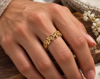 May include: A gold-toned ring featuring a continuous band of interconnected leaf-shaped cutouts. The metal has a polished finish, and the design wraps around the finger in a repeating pattern of small, open-work botanical shapes.