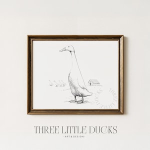 May include: A framed black and white print depicting a detailed illustration of a duck in a field, with smaller ducks and a small building in the background. The print is in a brown frame, and the text "THREE LITTLE DUCKS - ART & DESIGN -" is at the bottom.