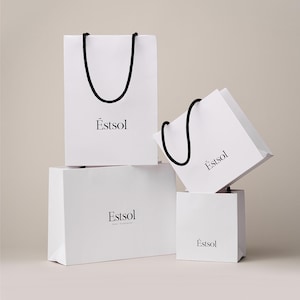 Peut inclure: Quatre sacs en papier blancs de diff&eacute;rentes tailles sont empil&eacute;s. Chaque sac est dot&eacute; d'une poign&eacute;e en corde noire et du mot "Estsol" imprim&eacute; en noir. Les sacs sont dispos&eacute;s sur un fond neutre.
