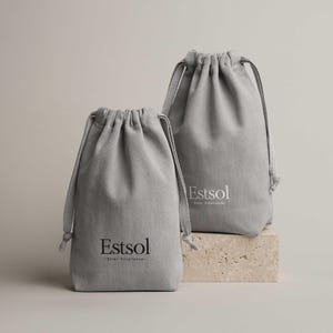 May include: Two gray drawstring bags with the word "Estsol" printed in white. The bags are made of a textured fabric and are displayed on a small, light-colored block. The bags have a simple, minimalist design.