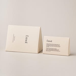 Pu&ograve; includere: Due scatole triangolari in cartone color crema con testo nero. La scatola pi&ugrave; grande presenta il nome del marchio Estsol e la frase Endow with uniqueness and beauty. La scatola pi&ugrave; piccola mostra il nome e un paragrafo di testo descrittivo.