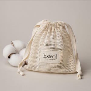 May include: A cream-colored mesh drawstring bag with the text "Estsol - Solar Excellence" on a rectangular label. A fluffy cotton boll is next to the bag. The bag is made of a woven material and has a drawstring closure.
