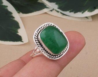May include: A silver ring featuring a large, rectangular, vibrant green gemstone. The gemstone is set in a decorative, rope-like border. The ring's band is a simple, split design, adding to its elegant appearance.