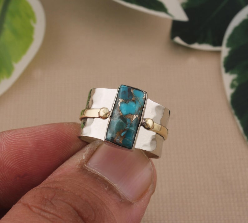 May include: Silver ring with a rectangular turquoise stone. The ring has gold accents and a hammered texture on the silver band. The turquoise stone has a mix of blue and brown colors.