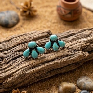 May include: A pair of stud earrings featuring clusters of four teardrop-shaped turquoise stones set in silver-toned metal. Each earring displays a central round turquoise stone surrounded by three smaller teardrop stones in a fan-like arrangement.