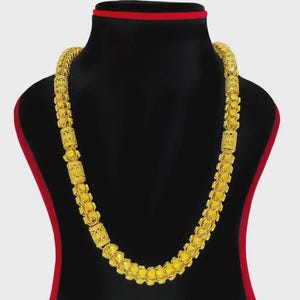 Puede incluir: Un collar de cadena dorada con un patrón repetitivo de eslabones cilíndricos texturizados que se alternan con eslabones circulares lisos. El collar tiene un acabado en oro amarillo brillante y se exhibe en un soporte de joyería negro.