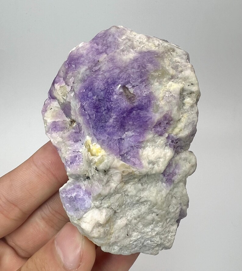 May include: A natural fluorite specimen, displaying a mix of colours. The stone has a central area of deep purple, set within a matrix of white and pale yellow. The rough texture and colour variations make it a captivating mineral for collectors.