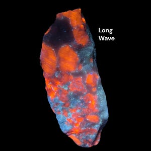 May include: A glowing, irregularly shaped rock against a black backdrop. The rock displays a vibrant orange and blue colour scheme, with the text "Long Wave" in white. The rock's surface has a textured appearance.
