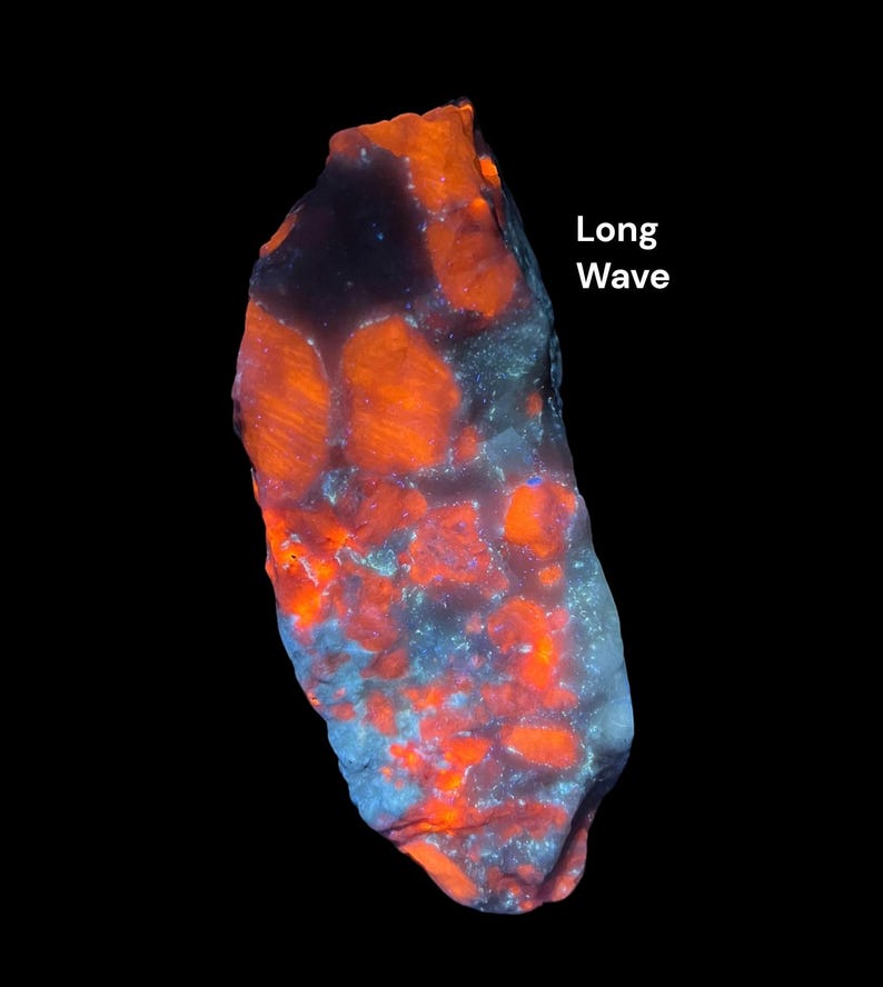 May include: A glowing, irregularly shaped rock against a black backdrop. The rock displays a vibrant orange and blue colour scheme, with the text "Long Wave" in white. The rock's surface has a textured appearance.