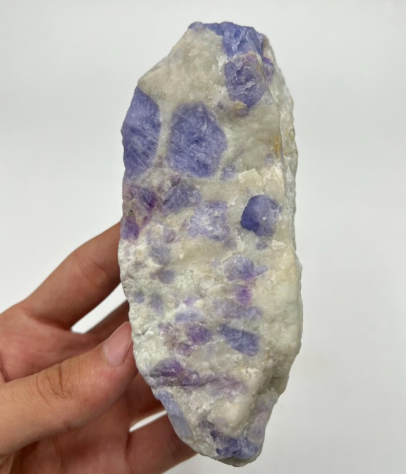 May include: A natural stone with a mix of white and purple colours. The stone has a textured surface with irregular shapes and sizes of purple inclusions. The overall appearance is a blend of colours and textures.
