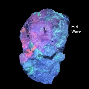 May include: A brightly illuminated rock formation against a black backdrop. The rock exhibits a spectrum of colours, including purple, blue, green, and orange. The text "Mid Wave" is displayed on the right side of the image.