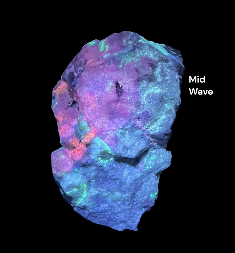 May include: A brightly illuminated rock formation against a black backdrop. The rock exhibits a spectrum of colours, including purple, blue, green, and orange. The text "Mid Wave" is displayed on the right side of the image.