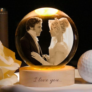 Könnte beinhalten: Beleuchtete Kristallkugel mit einem Sepia-Bild eines Paares in formeller Kleidung. Die Kugel steht auf einem Holzsockel mit der Aufschrift "I love you...". Ein weißer Golfball und eine gelbe Rose sind in der Nähe.