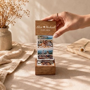 May include: A small wooden box with a hinged lid that pulls upwards to reveal an accordion-style photo strip. The lid is engraved with the text Alice Michael and the date 18.05.2026. The photo strip displays four distinct colour photographs.