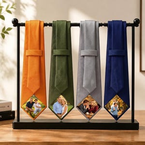 Può includere: Un espositore in metallo nero che sostiene quattro cravatte nei colori arancione, verde oliva, grigio chiaro e blu navy. Ogni cravatta presenta un taglio triangolare sul fondo che rivela una diversa fotografia di persone all'aperto.