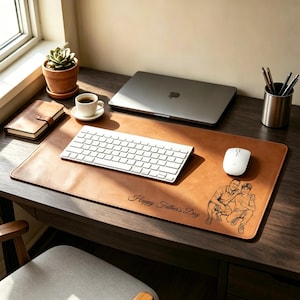 Op de afbeelding: Een bruine, rechthoekige bureauonderlegger met een in laser gegraveerde illustratie van twee personen en de tekst Happy Father's Day. De mat ligt op een donkerhouten bureau onder een wit computertoetsenbord en een computermuis.