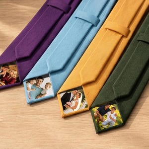 May include: Four neckties in purple, light blue, mustard yellow, and dark green, each featuring a custom rectangular photo print on the inner lining. The ties are arranged diagonally, showcasing a smooth fabric texture and a classic pointed tip.