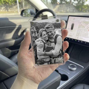 Peut inclure: Un clip de pare-soleil rectangulaire en acrylique transparent présentant une photographie en noir et blanc d'un couple qui s'enlace. Le texte Drive Safe est imprimé en haut et Always with you en bas, avec une petite icône de cœur.