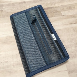 May include: A blue and gray striped clutch with a zippered pocket and a leather trim. The clutch has a white label with the text "Great Lakes" on it.