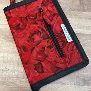 May include: A red zippered pouch with a black trim and a floral pattern. The pouch has a zippered pocket on the front and a label that reads "Grace's Cases".