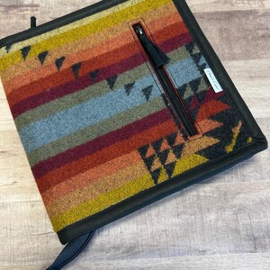 May include: A black zippered pouch with a colorful woven pattern. The pouch has a small zippered pocket on the front and a black zipper pull.