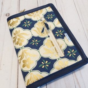 Puede incluir: Una funda para cuaderno con cremallera azul marino con un patrón floral dorado y verde. La funda tiene un bolsillo con cremallera en la parte delantera y una etiqueta que dice "Emma's Creations".