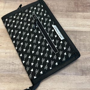 Puede incluir: Cartera negra con cremallera, patrón de flechas blancas y una etiqueta plateada que dice "Gracie Cakes".