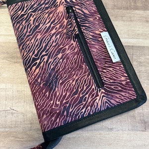 May include: A black zippered pouch with a brown and black patterned fabric. The pouch has a zippered pocket on the outside and a black label with the text "Grace's Cakes".