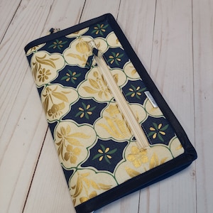 Puede incluir: Una bolsa con cremallera azul marino con un tejido estampado en oro y blanco con un diseño geométrico. La bolsa tiene una cremallera y una pequeña etiqueta que dice "Laura Craft".